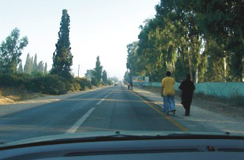 כביש כפרי ללא מדרכה עם שני הולכי רגל צועדים על שוליו.