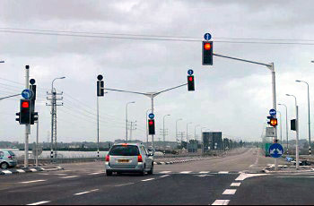 צומת עירוני מרומזר עם מספר עמודי רמזור מעל הכביש ורכב ממתין בפני האור האדום.