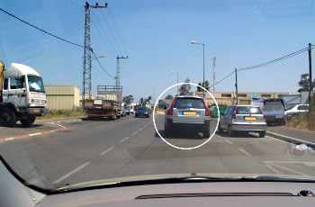 רחוב עם רכב כסוף חונה בחנייה כפולה (מסומן בעיגול) ומשאית מתקרבת בנתיב הנגדי.