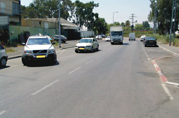מבט מתא נהג משאית: רכב לבן יוצא מחניה לכביש עירוני עם רכבים נוספים.