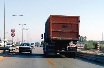 כביש בין-עירוני עם משאית כתומה גדולה הנכנסת לנתיב הנסיעה, ותמרור מהירות מוגבלת 60 בצד.