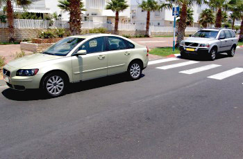 רכב ירקרק חונה צמוד למעבר חצייה מסומן, ורכב לבן/כסוף חונה במרחק אחריו.