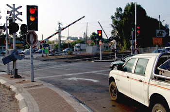 מפגש מסילת ברזל עם מחסום ורמזור אדום דולק, רכב לבן ממתין.