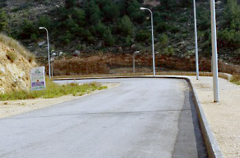 דרך הררית מתפתלת עם עקומה חדה, מדרון חשוף בצד ועמודי תאורה לאורך השוליים.