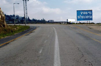 כביש מתעקל בסמוך למעבר עילי (גשר), עם שלט הסברה כללי בצד.