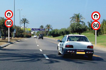 שני תמרורי מהירות מרבית 80 קמ״ש בעיגול אדום, ולצידם שלט כחול עילי עם שמות יישובים.