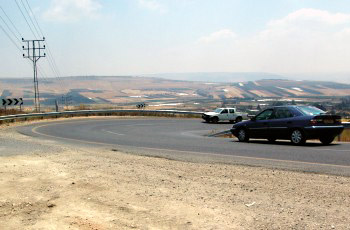 רכב כהה ורכב לבן מתקרבים זה לזה בתוך עקומה חדה בכביש הררי.