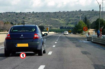 רכב כחול בנתיב הימני של כביש, שמים מעוננים, ללא אורות דולקים.