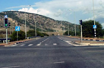 צומת רב-נתיבי בין הרים, רמזורים אדומים משני צדי הכביש, שלט כחול עם חץ הכוונה לנתיבים