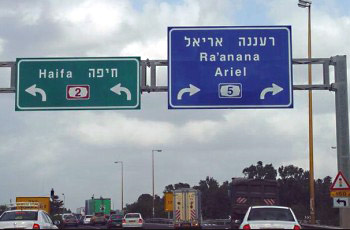 שני שלטי הכוונה מעל הכביש - שלט ירוק לחיפה (כביש 2) פונה שמאלה, שלט כחול לרעננה/אריאל (כביש 5) פונה ימינה