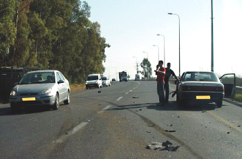 תאונת דרכים: שני אנשים עומדים ליד רכב כסוף בכביש, רכבים נוספים בנתיב הנגדי