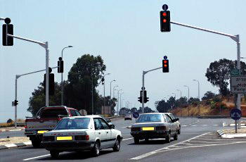 צומת עם שני רמזורים באור אדום, רכבים ממתינים, טנדר אדום ושתי מכוניות כסופות